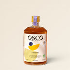 Livvy OSCO L'Original organic non-alcoholic aperitif bottle with award seals on a sunny outdoor table.