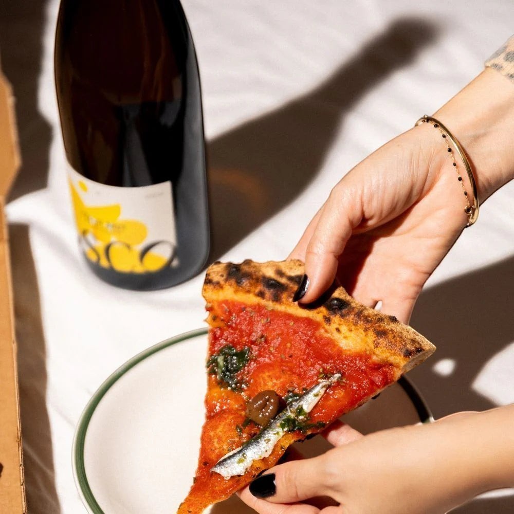 OSCO L'Éclat Brut sparkling drink bottle served with a slice of pizza on a white plate.