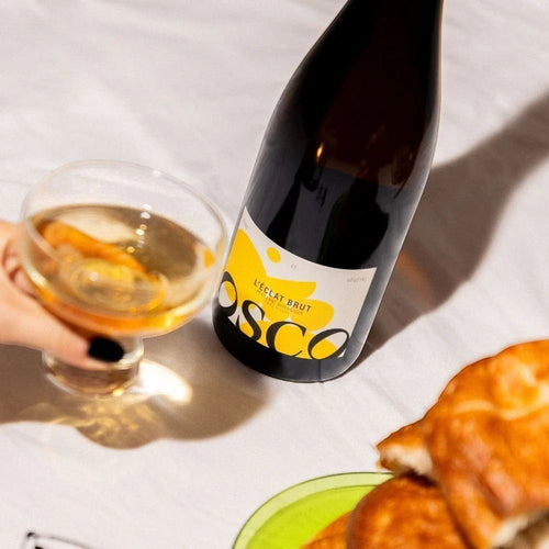OSCO L'Éclat Brut non-alcoholic sparkling drink bottle next to a glass and pastries on a white tablecloth